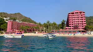 A pink hotel with multiple balconies, a beach, and several boats in the water.