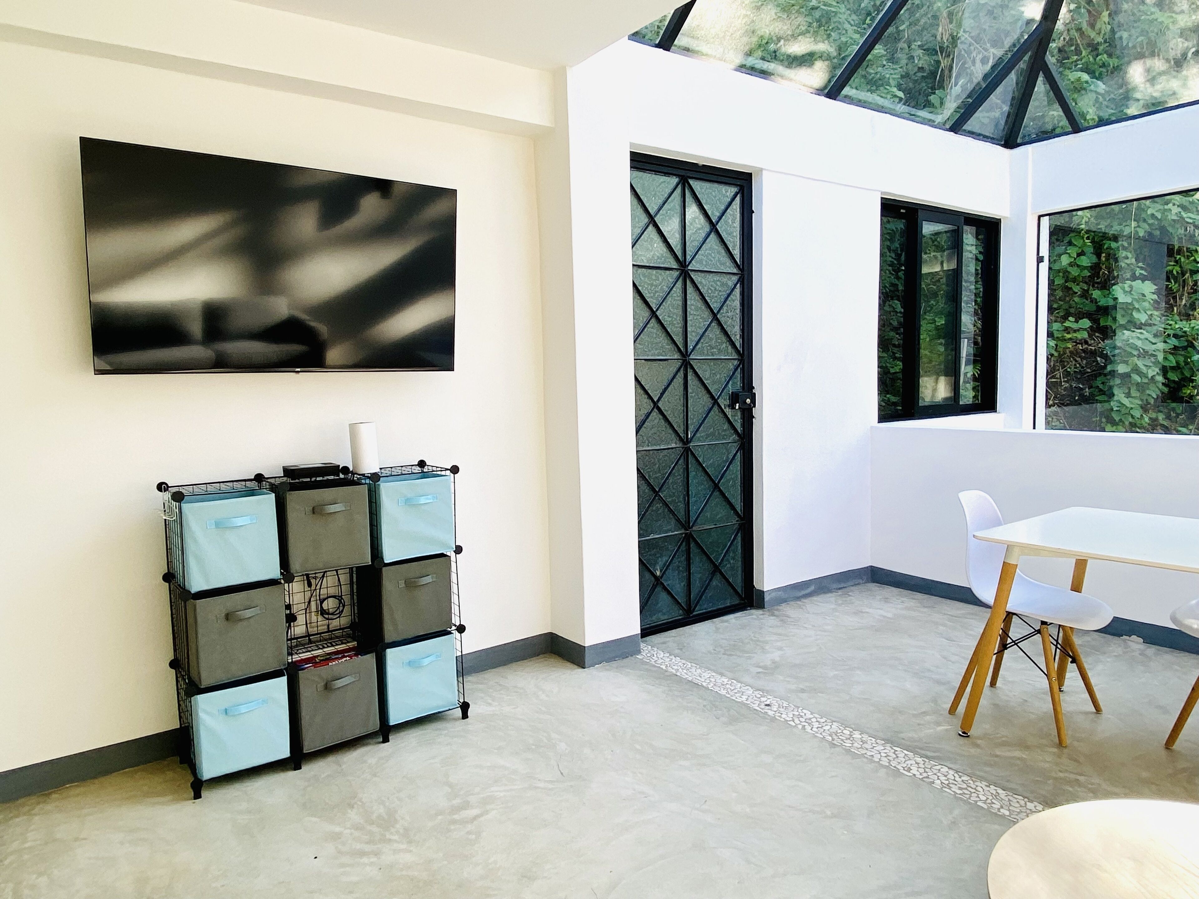 A modern interior with a flat-screen TV, storage units, a dining area with a table and chairs, and a glass door leading outside.