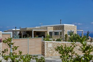 Une maison moderne à deux étages, dotée d’une façade en pierre, de grandes fenêtres et offrant une vue sur la mer.
