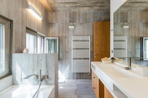 Ein modernes Badezimmer mit Holzboden, einem großen Spiegel, einer Badewanne und einem Waschtisch mit Spüle und Handtuchhalter.