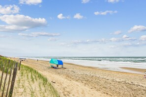 A beach with a wooden fence, a blue umbrella, and the ocean.
