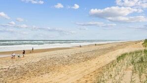 Una playa con gente caminando, una orilla arenosa y el océano.
