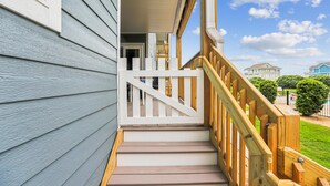 A wooden staircase leading to a porch with a white railing, a clear sky, and a residential neighborhood in the background. - Heaven's Nest -- First Floor Duck Condo with direct access to Beach and Pool (Kitty Hawk)