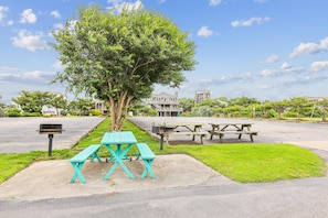 Un’area pic-nic con panchine e un albero, circondata da un parcheggio e edifici residenziali.