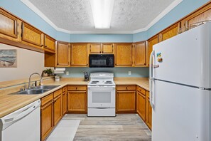 A kitchen with wooden cabinets, a white refrigerator, a microwave, a stove, and a sink. - Heaven's Nest -- First Floor Duck Condo with direct access to Beach and Pool (Kitty Hawk)