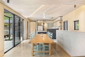 Relax in this open-plan living space with a central dining table and sliding glass door leading to a garden view.