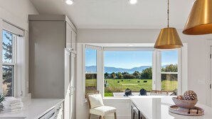 A modern kitchen with a large window, white cabinetry, and a view of a green landscape. - Gateway to Bear Lake (Sleeps 19) (Garden City)