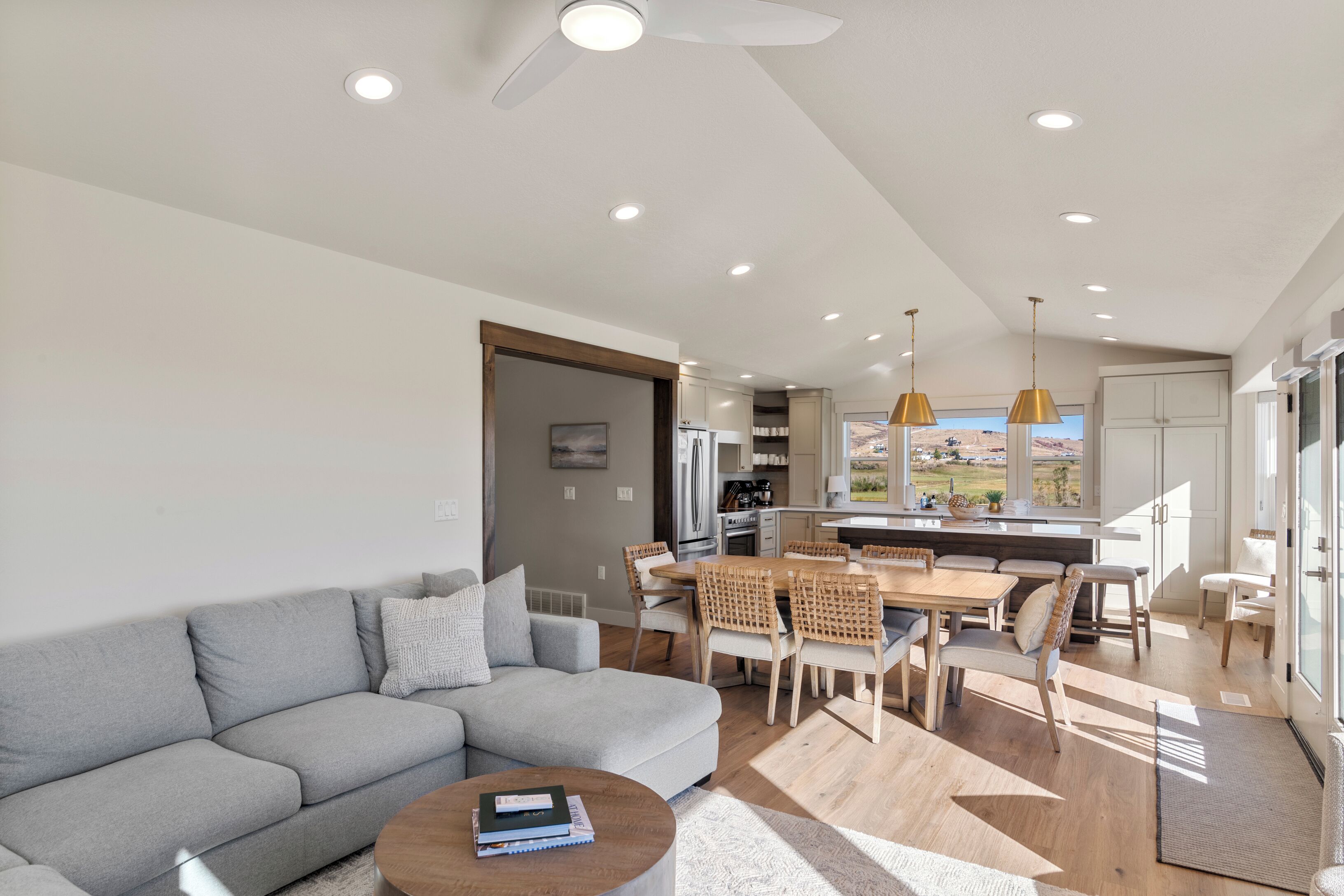 A modern living room with a grey sofa, a coffee table, and a dining area with wooden chairs and a table.