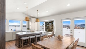 A modern kitchen with a large island, bar stools, and a dining table with chairs. - Gateway to Bear Lake (Sleeps 19) (Garden City)