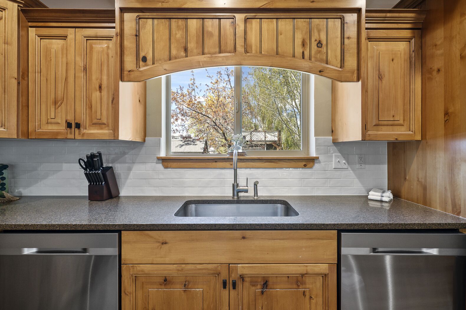 Una cocina con armarios de madera, un lavamanos de acero inoxidable y una ventana con vistas a árboles.