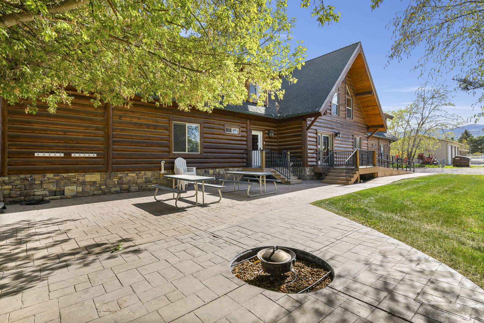 Una cabaña de troncos con base de piedra, un patio con mesas de picnic y un brasero.
