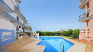 Uma piscina com interior azul, rodeada por um espaço pavimentado com um salva-vidas e uma placa.