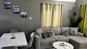 A modern living room with a grey sofa, a white marble table, and a green curtain. - Sky View Villas @ Edmund Ridge Estate (Montego Bay)