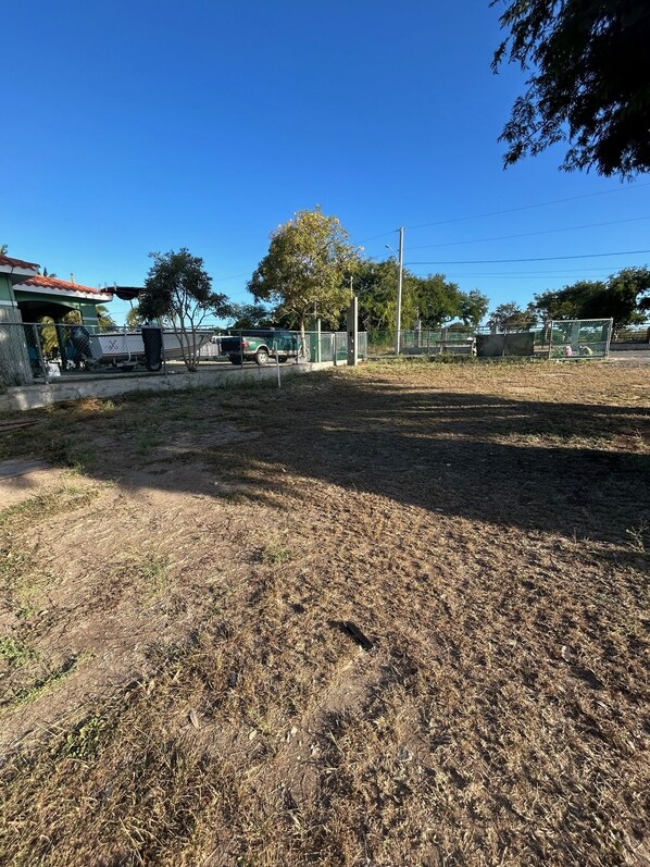 Ein eingezäunter Außenbereich mit trockenem Gras, einem geparkten Fahrzeug und einem Gebäude mit rotem Dach.