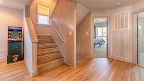 A wooden staircase with a game console in the corner, a door leading to another room, and a window with blinds.