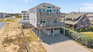 A two-story beachfront house with a balcony, a covered porch, and a view of the beach.