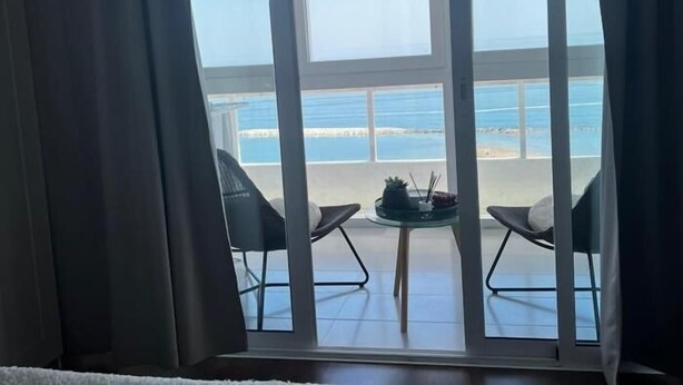 A room with a large window overlooking a beach. There are two chairs and a small table with a plant and a candle.