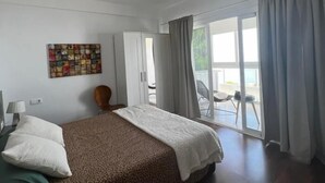 A hotel room with a bed, a ceiling fan, a wardrobe, a chair, a table, and a view of the outside.
