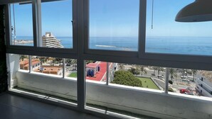 A room with large windows overlooking a coastal area, featuring a view of the sea and buildings.
