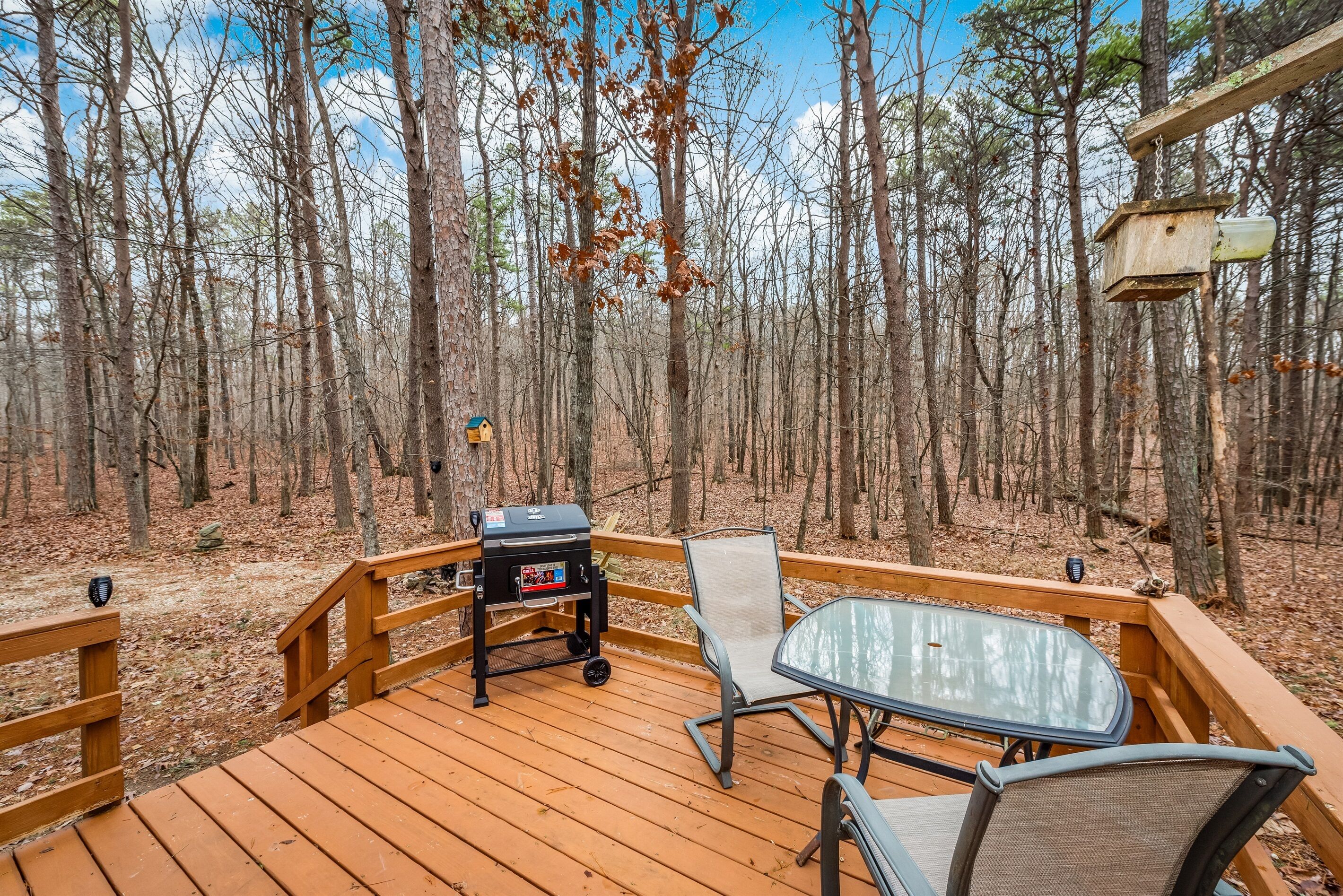 A wooden deck with a grill, a glass table, and two chairs.