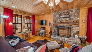 A cozy cabin interior with a stone fireplace, wooden walls, and a ceiling fan. - Deerwood-private, cozy cabin in the woods (Mentone)