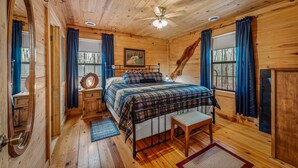 A wooden cabin bedroom with a bed, bench, and a ceiling fan. - Deerwood-private, cozy cabin in the woods (Mentone)