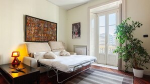 A bedroom with a bed, a nightstand, a lamp, a radiator, a window, and a potted plant.