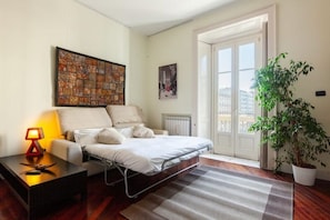 Quarto com cama, mesa de cabeceira, abajur, radiador, janela e planta em vaso.