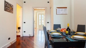 A dining area with a table set for four, a bottle of wine, and fruit on the table.