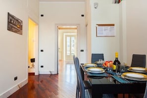 Uma sala de jantar com uma mesa posta para quatro pessoas, uma garrafa de vinho e frutas sobre a mesa.