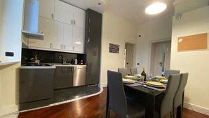 A modern kitchen with stainless steel appliances, a dining area with a black table and chairs, and a wooden floor.
