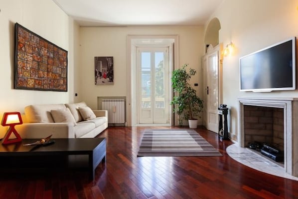 Uma sala de estar com sofá, mesa de centro, TV, lareira e porta que dá para outro cômodo.