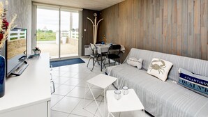 A modern living room with a sofa, a coffee table, and a dining area with chairs and a table. - Galv Ar Mor, Petite Maison Cosy Proche Plage (Cléder)