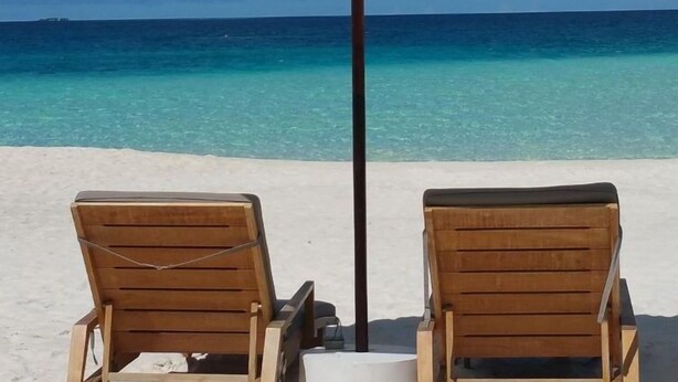 Two wooden lounge chairs under a white umbrella on a beach with clear blue water and a clear sky. - Galv Ar Mor, Petite Maison Cosy Proche Plage (Cléder)