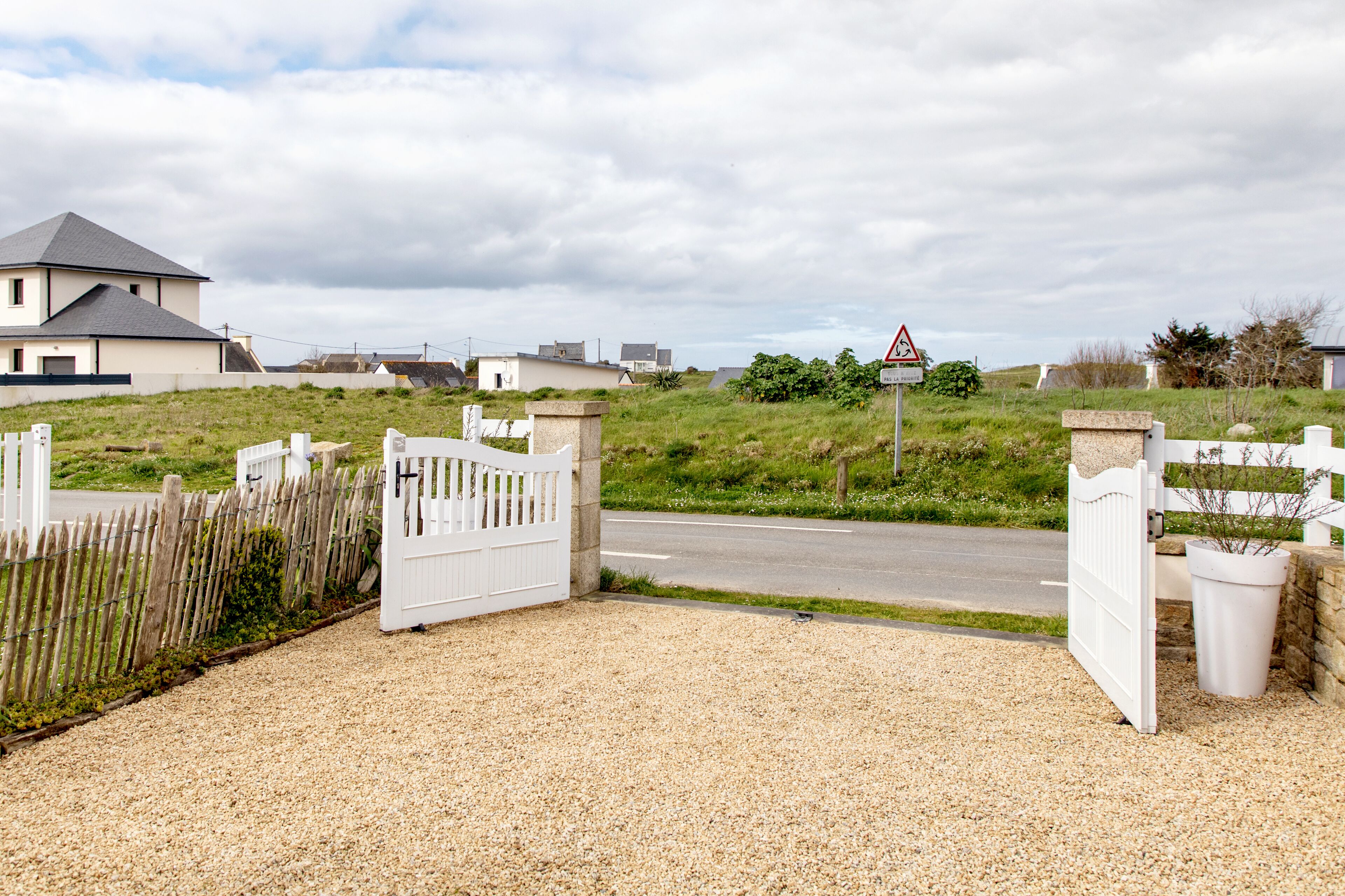 A gated driveway leading to a residential area with houses and a road.