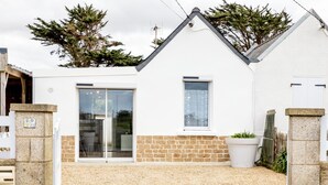 A white house with a stone foundation, a large window, and a door. - Galv Ar Mor, Petite Maison Cosy Proche Plage (Cléder)