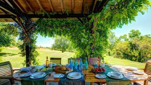 Un área de comedor al aire libre con mesas dispuestas para una comida, rodeada de follaje y árboles.