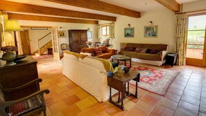 Un salón espacioso con escaleras, vigas de madera, un sofá, una mesa de centro y vistas a un jardín a través de una ventana.
