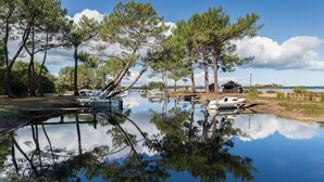 A serene lakeside setting with boats docked, trees reflecting on the water, and a small building in the background.