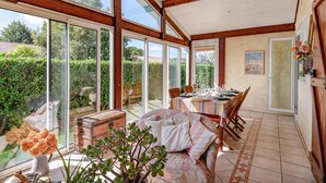 A sunroom with large glass doors, a dining table set for four, and a cozy seating area with a sofa and cushions.