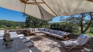 An outdoor seating area with a large umbrella, a sofa, a lounge chair, and a wine bucket.