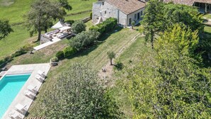 A stone house with a swimming pool, surrounded by green fields and trees.