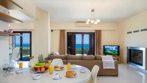 A modern living room with a dining area, a sofa, a TV, and a fireplace. - Iliada - Four Bedroom Villa, Sleeps 8 (Maleme)
