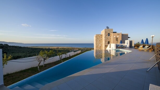 A modern pool area with a clear view of the sea, lounge chairs, and a stone building. - Iliada - Four Bedroom Villa, Sleeps 8 (Maleme)