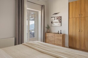 A bedroom with a bed, a wooden wardrobe, a window with curtains, and a painting on the wall.