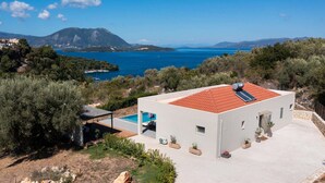 A modern villa with a swimming pool, surrounded by lush greenery and overlooking a large body of water. - Tina - Three Bedroom Villa, Sleeps 6 (Spartochori)
