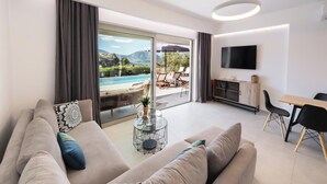A modern living room with a large window, a sofa, a coffee table, and a flat-screen TV. - Tina - Three Bedroom Villa, Sleeps 6 (Spartochori)