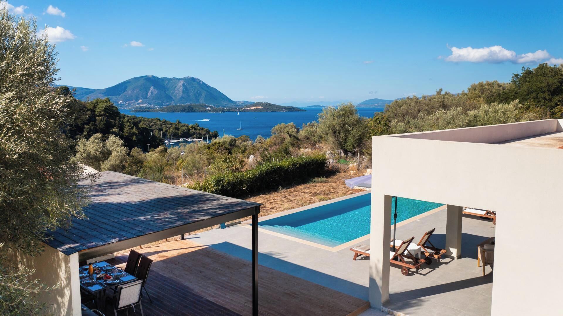 A modern villa with a swimming pool, outdoor seating, and a view of the sea and mountains.
