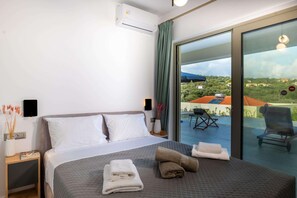 Relax in comfort with a large bed, bedside table, and sliding door leading to an outdoor area with pool and hilly views.