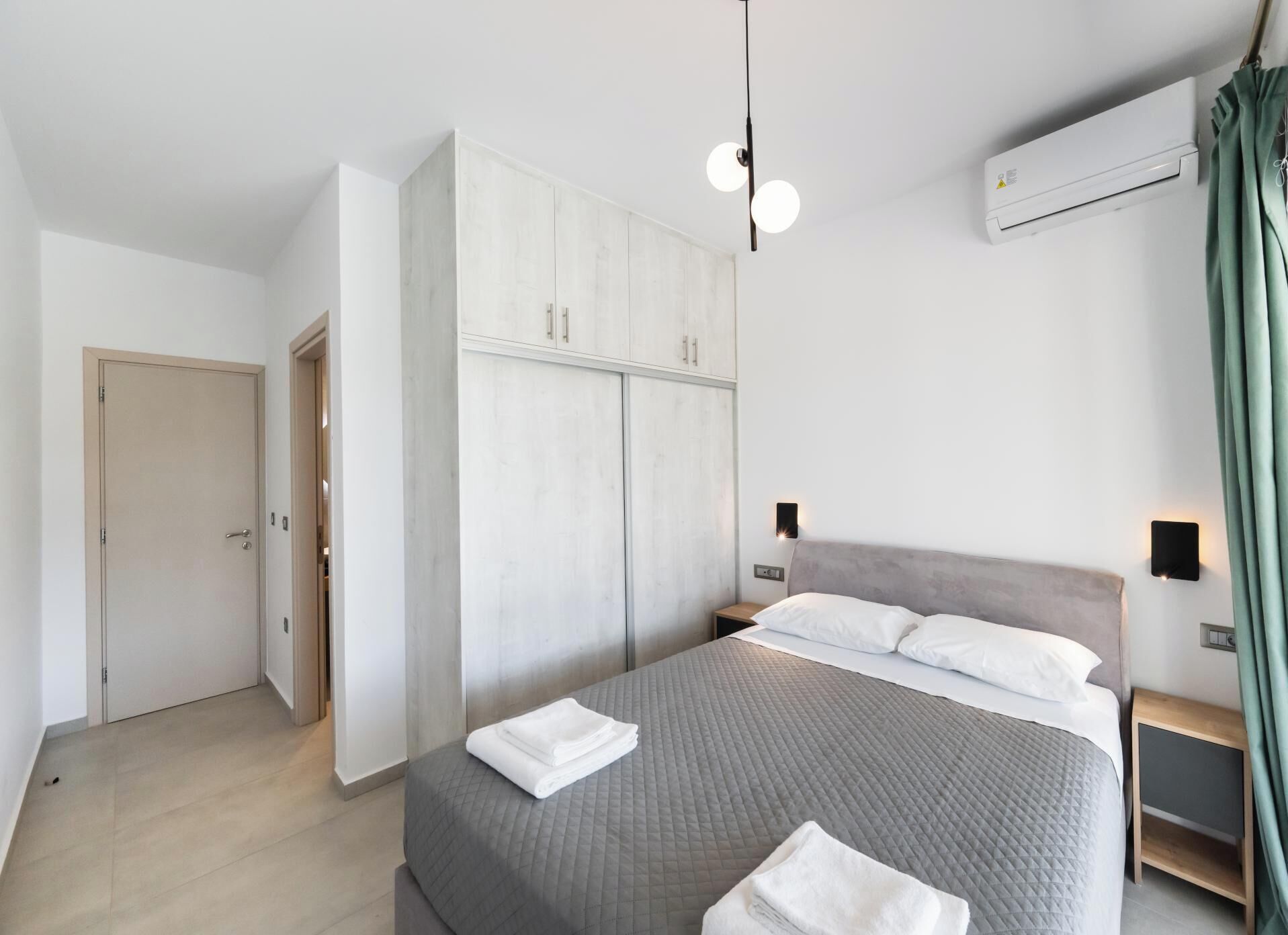 Ein modernes Schlafzimmer mit einem großen Bett, einem Kleiderschrank, einem Nachttisch und einer Klimaanlage.